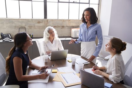 Businesswoman stands addressing female colleagues in meeting