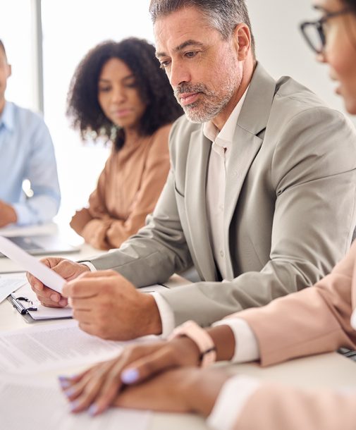 Busy senior Indian businessman investor bank client reading document at office team meeting with executive professional financial law experts group. Consultancy and advisory services, vertical shot.