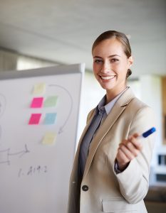 A young woman gesturing with her hand while standing in her office doing a presentation.