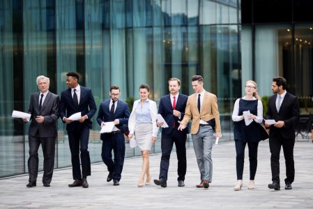 Several business people in elegant suits walking by modern building while having talk with each other